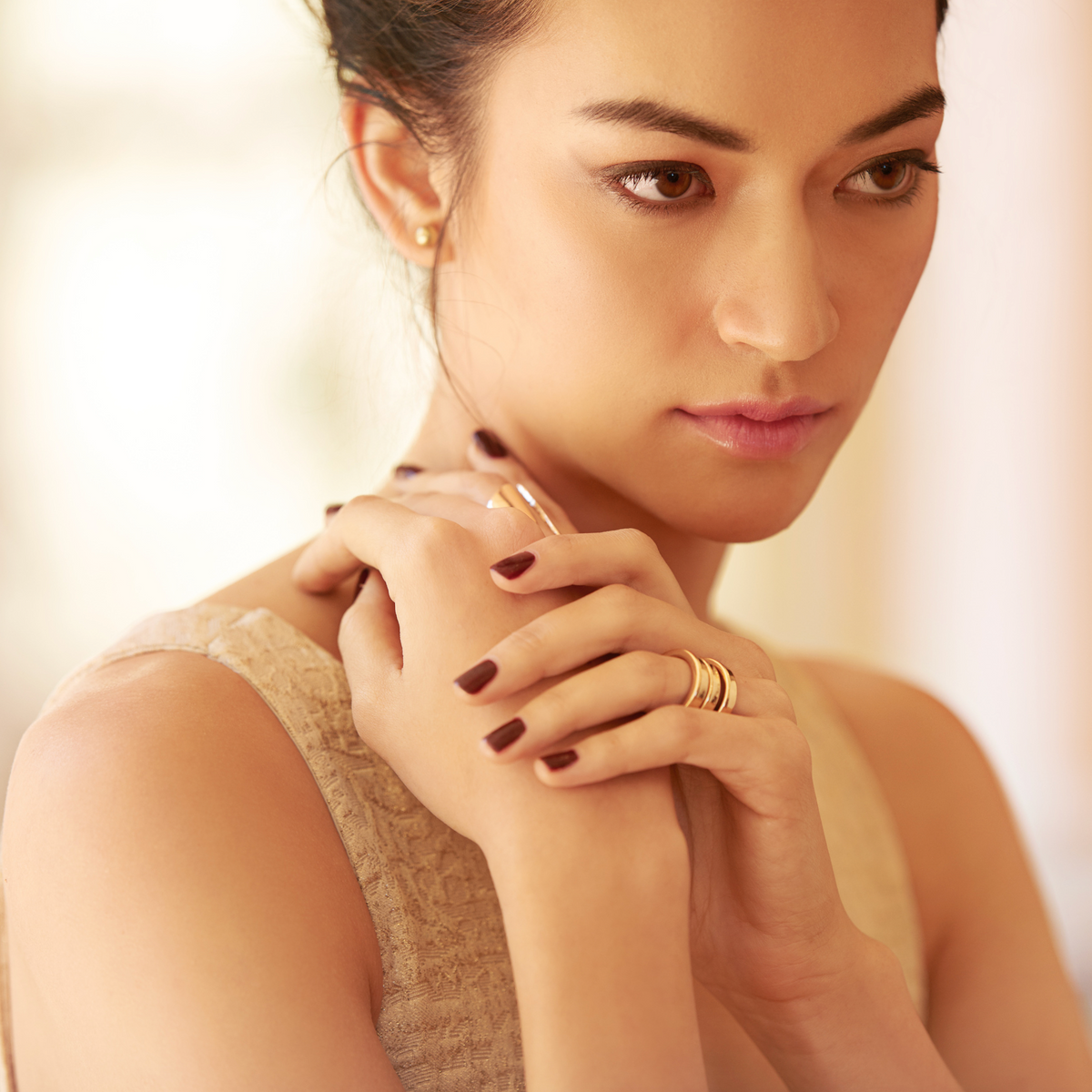 Woman with gold rings and burgundy nails resting her hands near her neck